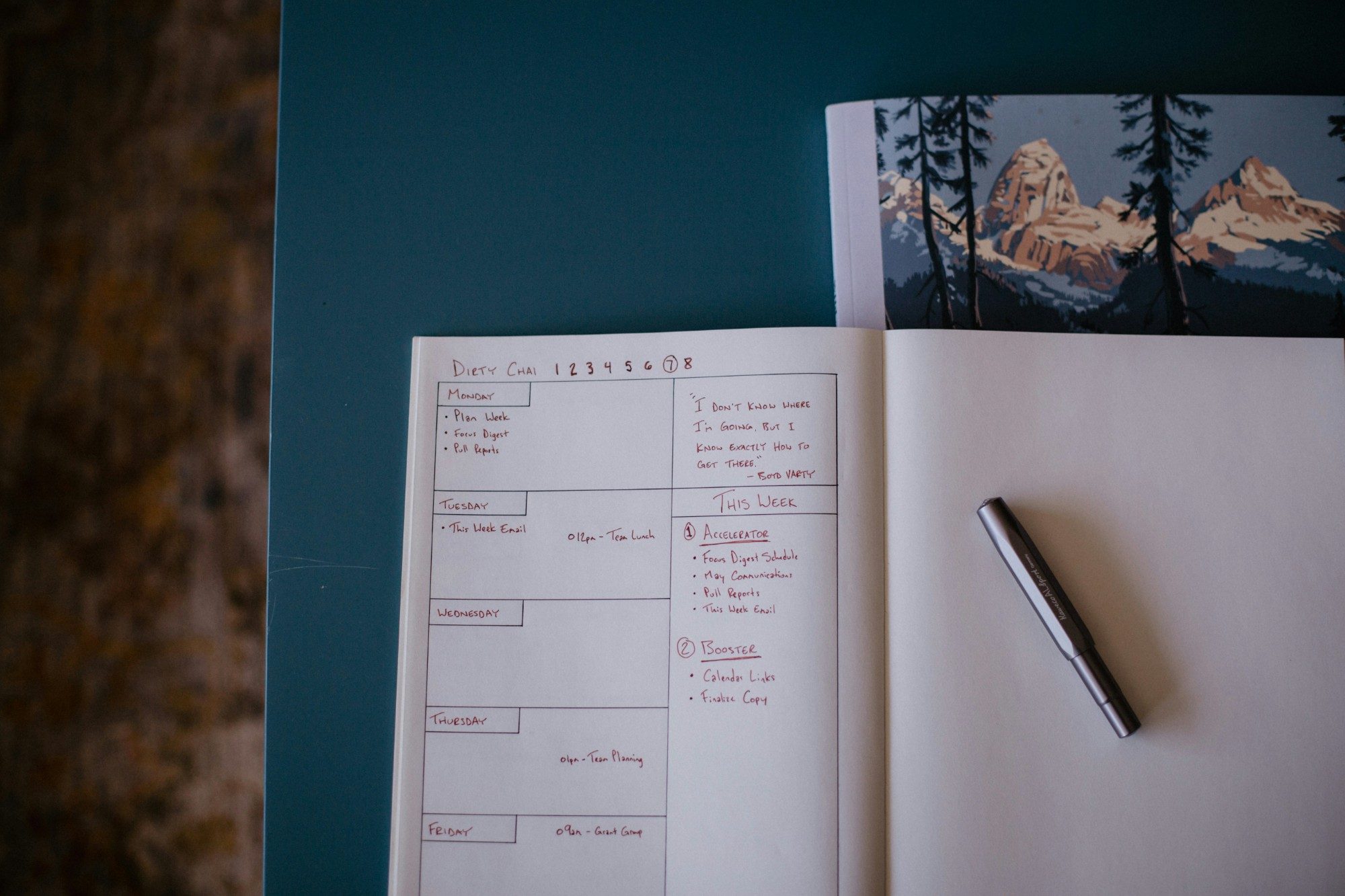 An open notebook with a handwritten weekly plan and a pen