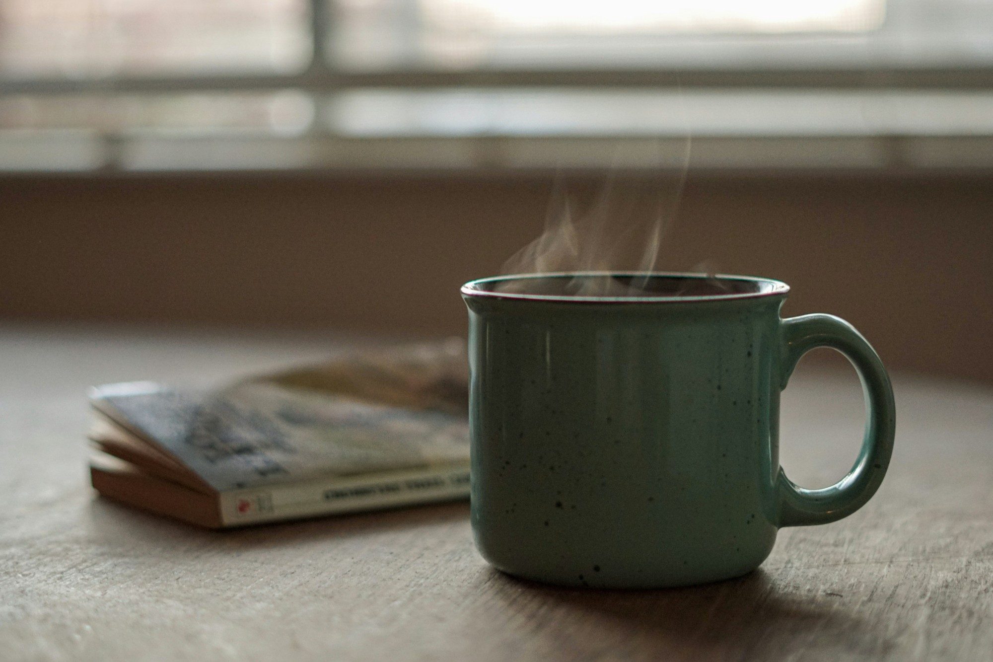 A steaming mug beside a closed book on a table