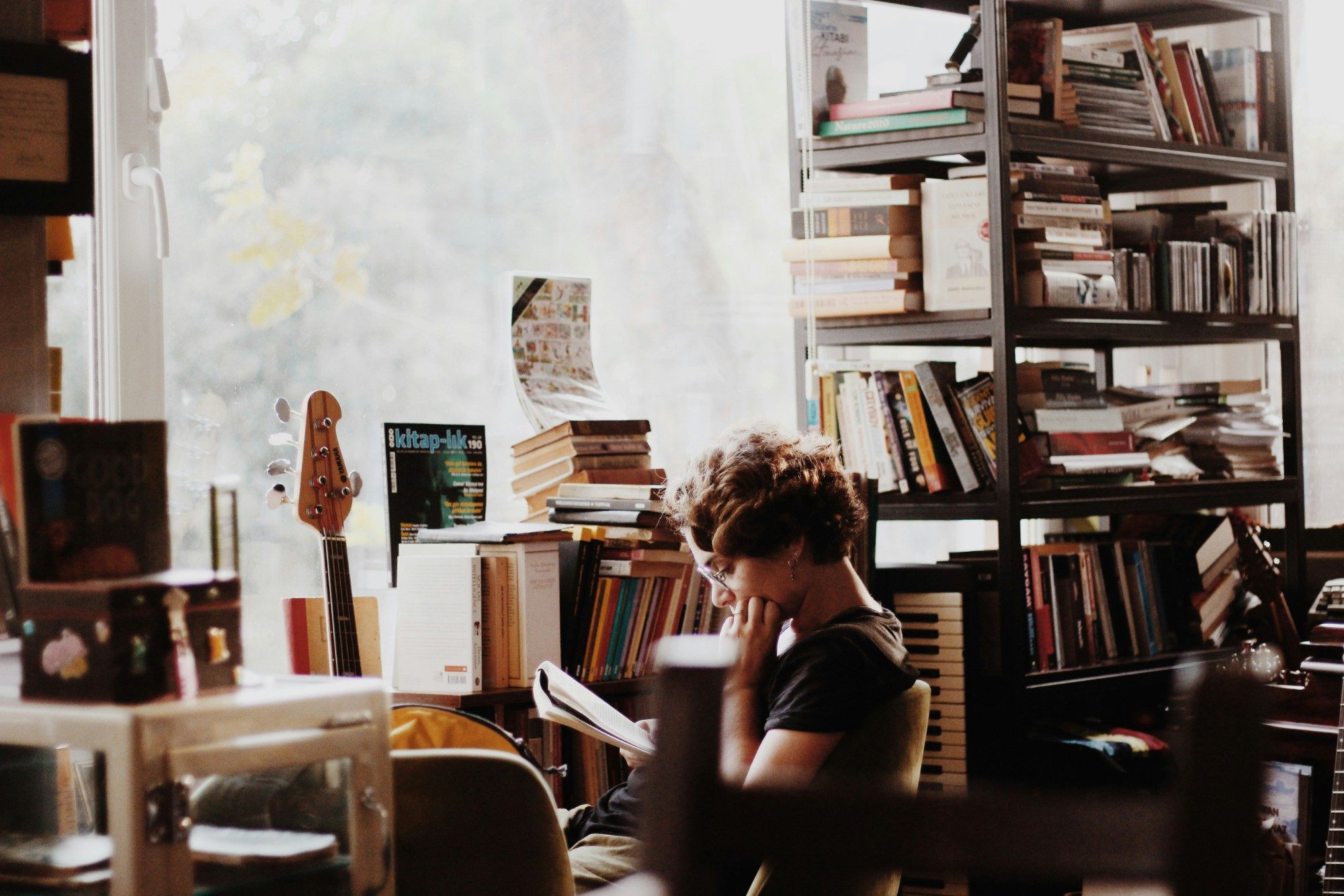 Someone reading among bookshelves by a bright window